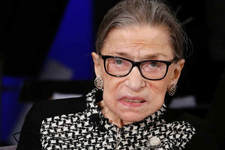 A close up shot of Ruth Bader Ginsburg, who is looking upwards through her glasses.