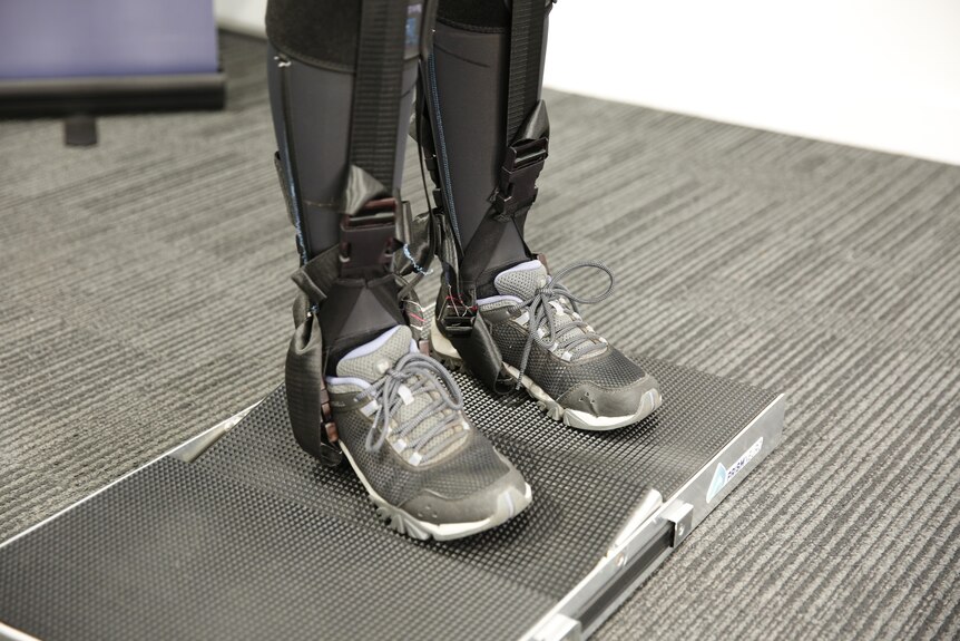 A close up photo of the lower half of a space suit, showing straps and elastic around sports shoes, standing on a scale.