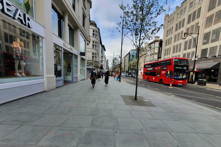 A handful of people walking on Oxford street as a red double decker bus goes past.