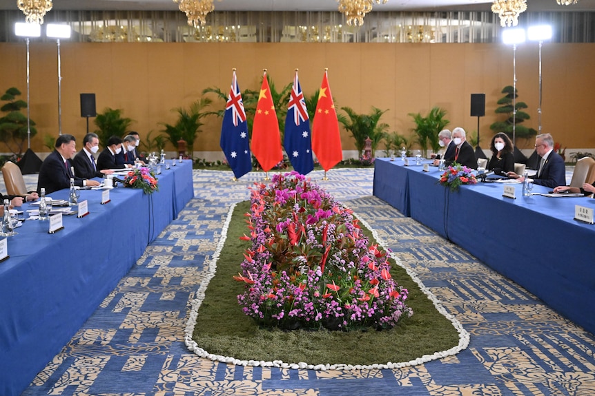 groups of people sat at two long blue tables with flowers and Australian and Chinese flags in the middle