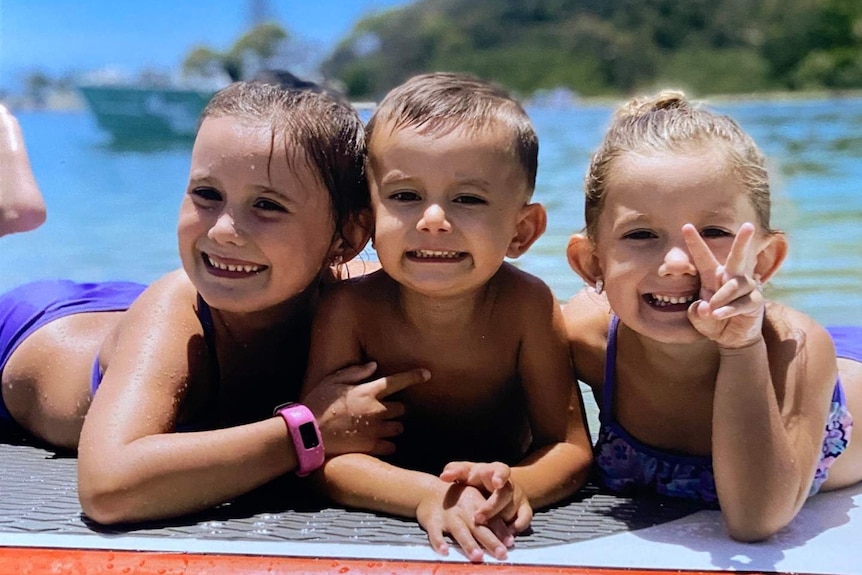 Three children on a surfboard in the ocean.