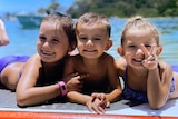 Three children on a surfboard in the ocean.