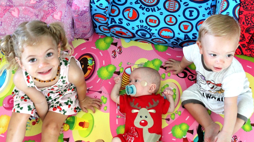 Three year old girl, seven month old boy and 18-mth old boy sit interacting on a mat.