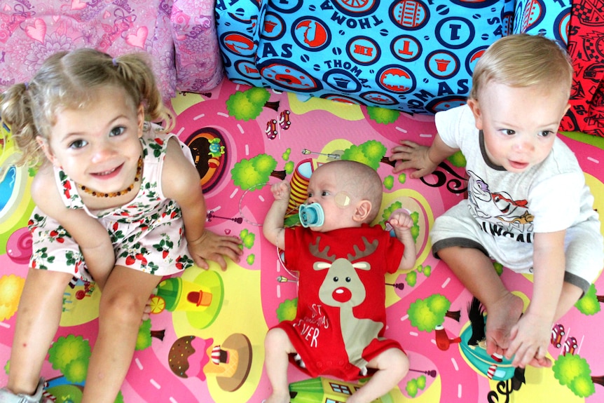 Three year old girl, seven month old boy and 18-mth old boy sit interacting on a mat.