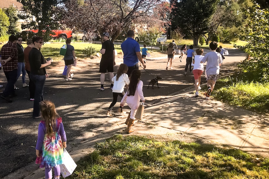 Several adults and children run through a suburban street hunting for Easter eggs.