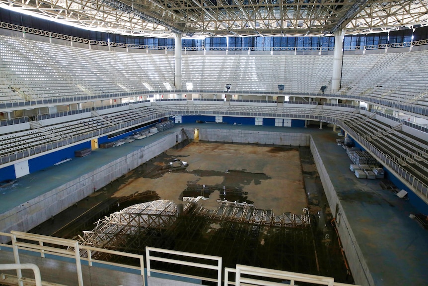 Inside a decaying aquatic stadium with an empty pool 