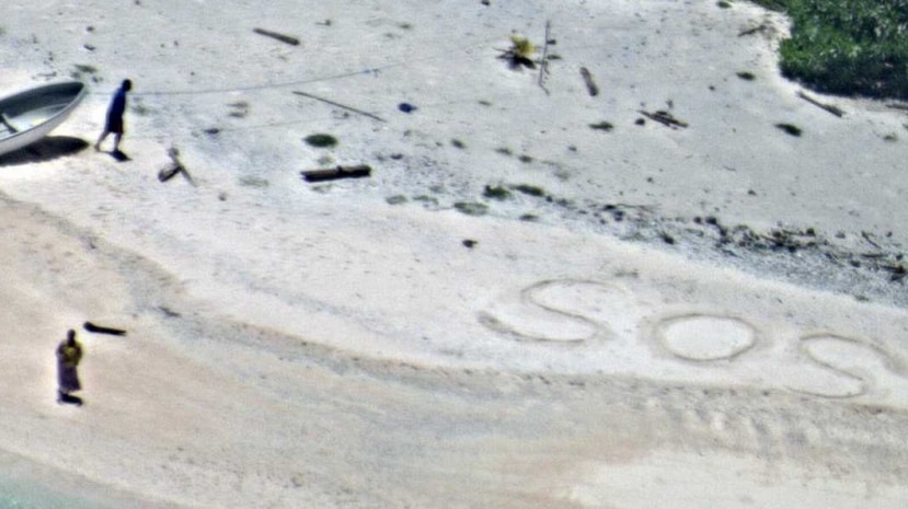 SOS written on a beach, with two people and a boat nearby.