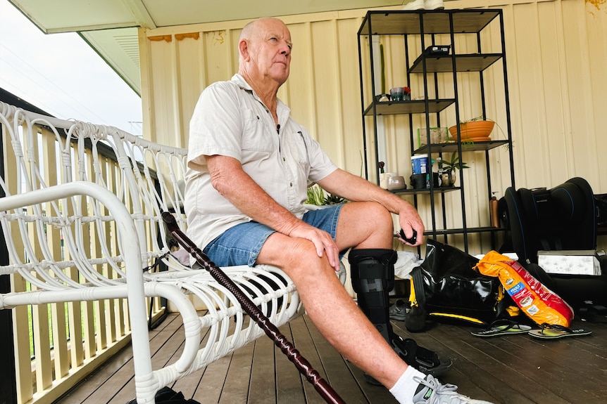 a man sitting in a chair on a deck with a knee cast