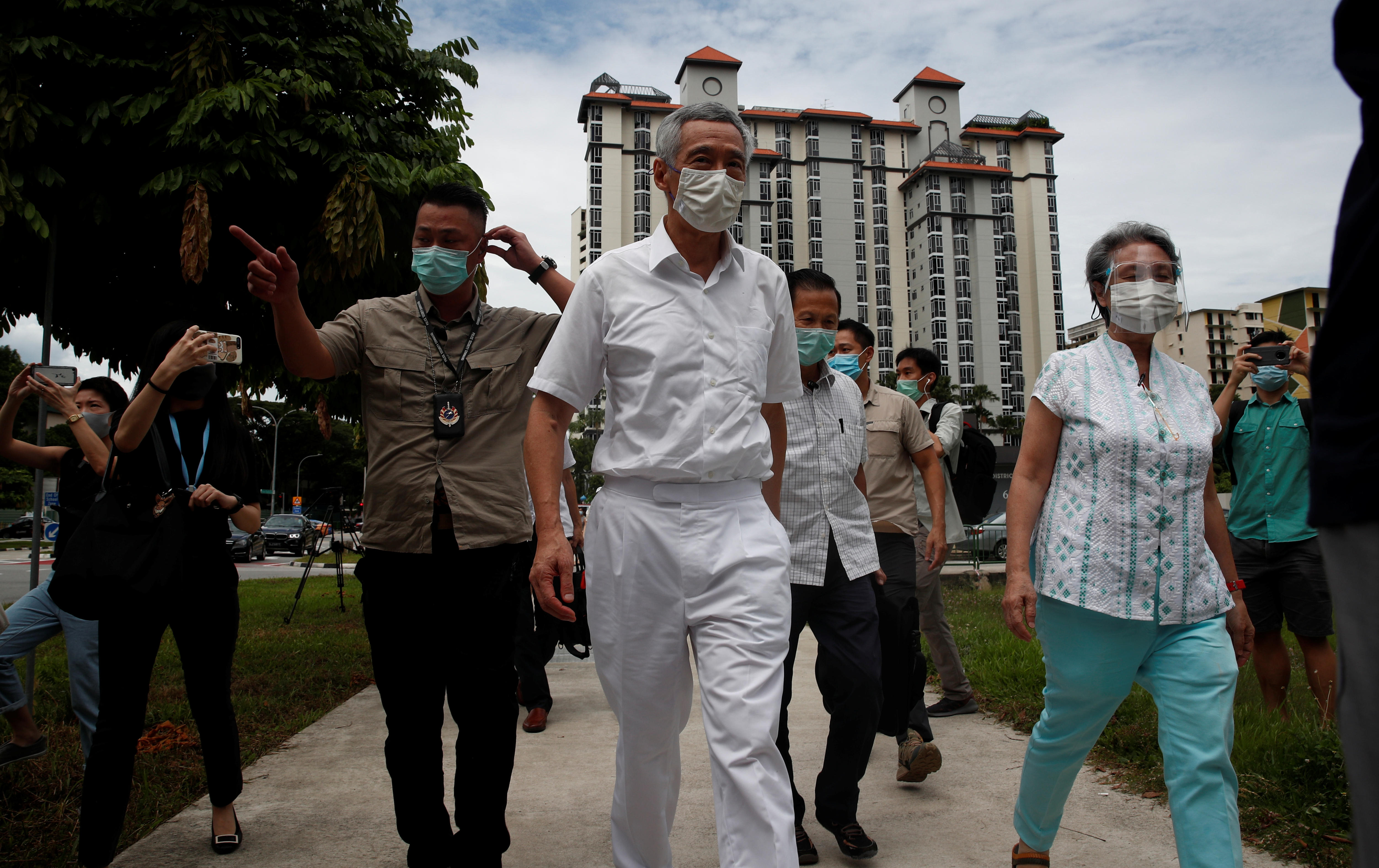 Lee Hsien Loong and his wife Ho Ching walk along a footpath with several other people, all in medical masks. 