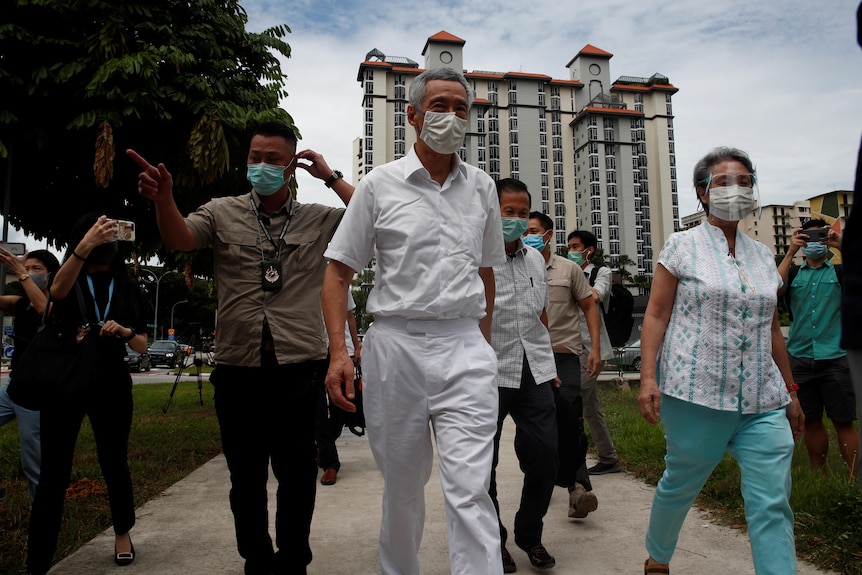Lee Hsien Loong and his wife Ho Ching walk along a footpath with several other people, all in medical masks. 