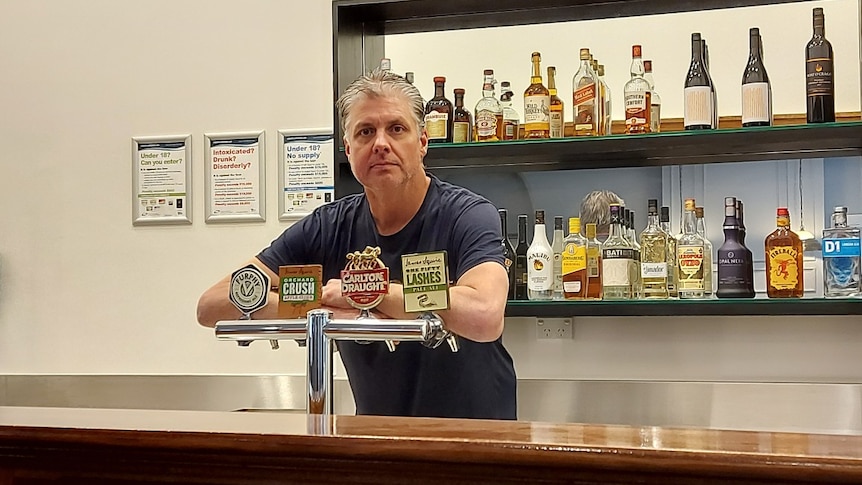 Peter leans over beer taps behind a bar.