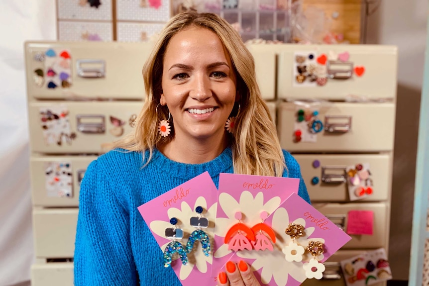 A woman holds three pairs of earrings out in front of her.