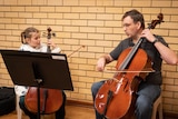 Two cellists side by side: one a young girl, the other a man.