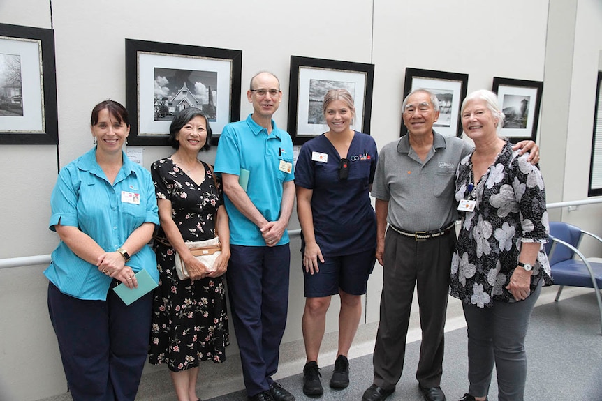 Two men and four women gathered in front of photos on a wall at a hospital