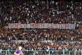 A stadium packed with thousands of people. They are holding a banner reading Genova merita giustizia (Genoa deserves justice).