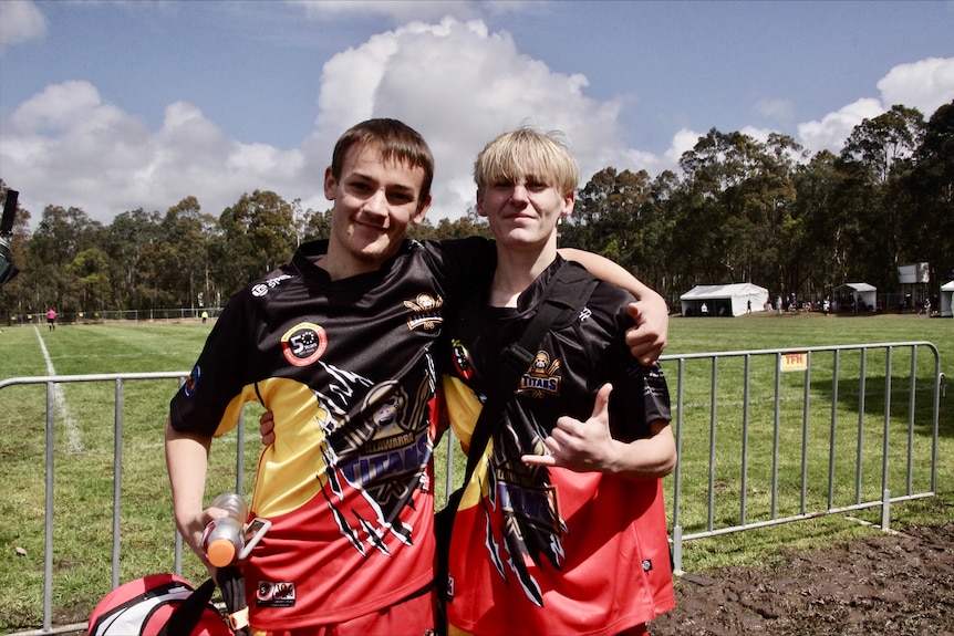 Two men wearing red, yellow and black rugby league jerseys with their arms around each other