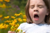 A girl sneezing while holding a bunch of flowers.