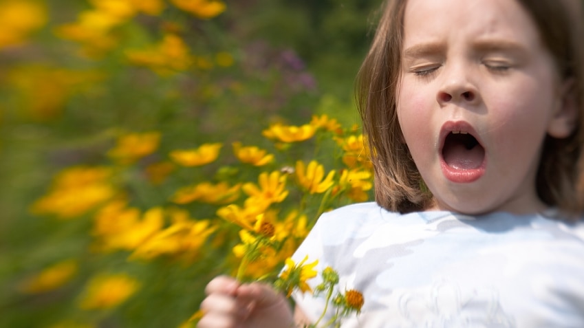 A girl sneezing while holding a bunch of flowers.