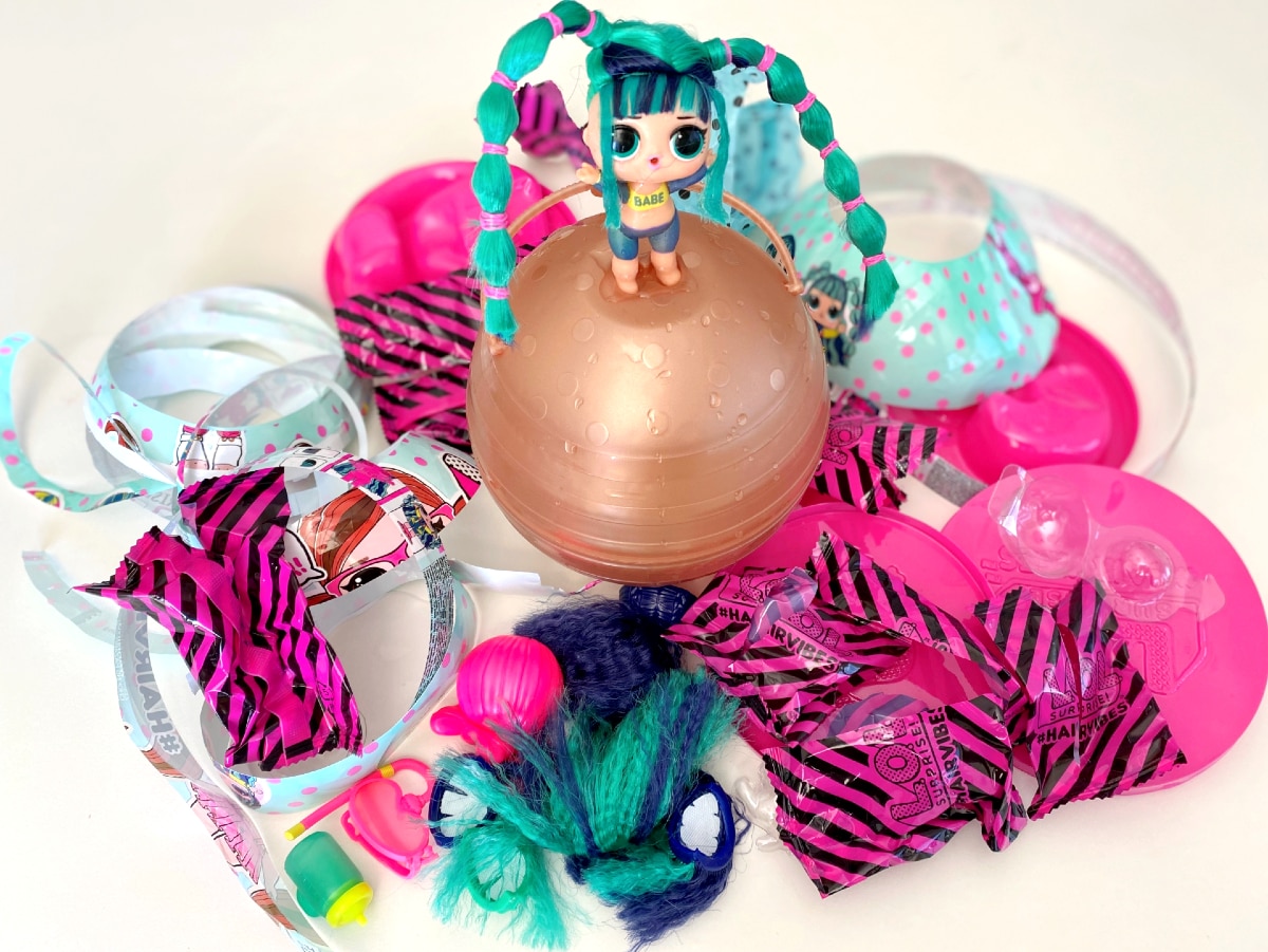 A doll stands less than 10cm tall with a lot of plastic wrapping all around it.