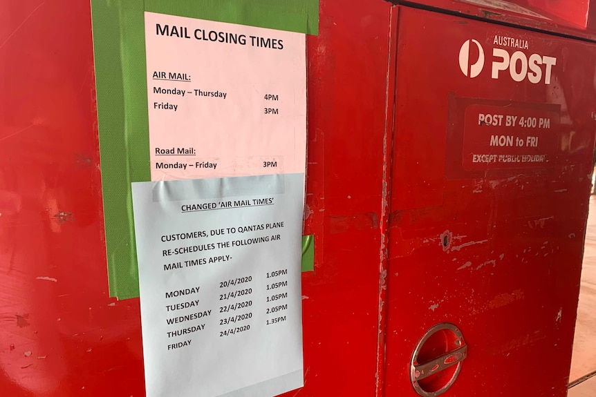 A bright red Australia Post letterbox with a schedule showing the mail closing times taped to it.