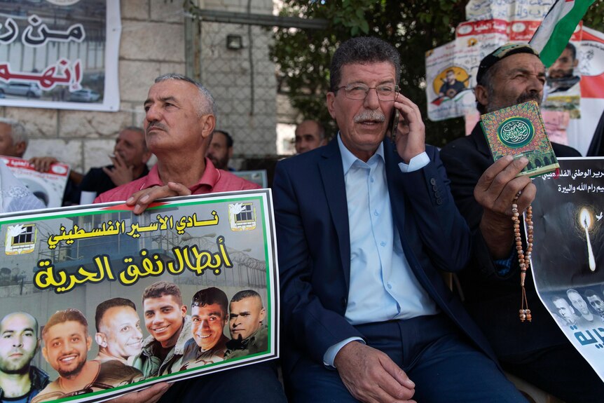 A Palestinian man talking on a mobile phone sits next to a poster of six men who escaped from an Israeli jail.