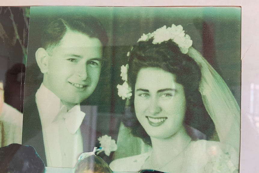 A black and white photograph of a woman with dark hair in a wedding dress and white veil standing next to a man in a suit.