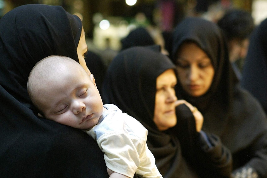 An Iranian baby sleeps on his mother's shoulder
