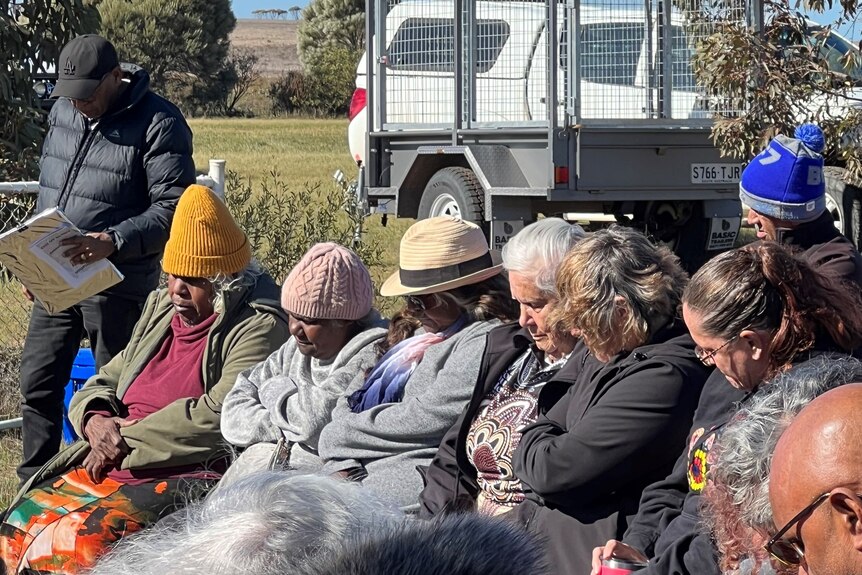 A group of people including Indigenous elders sitting with their heads buried.