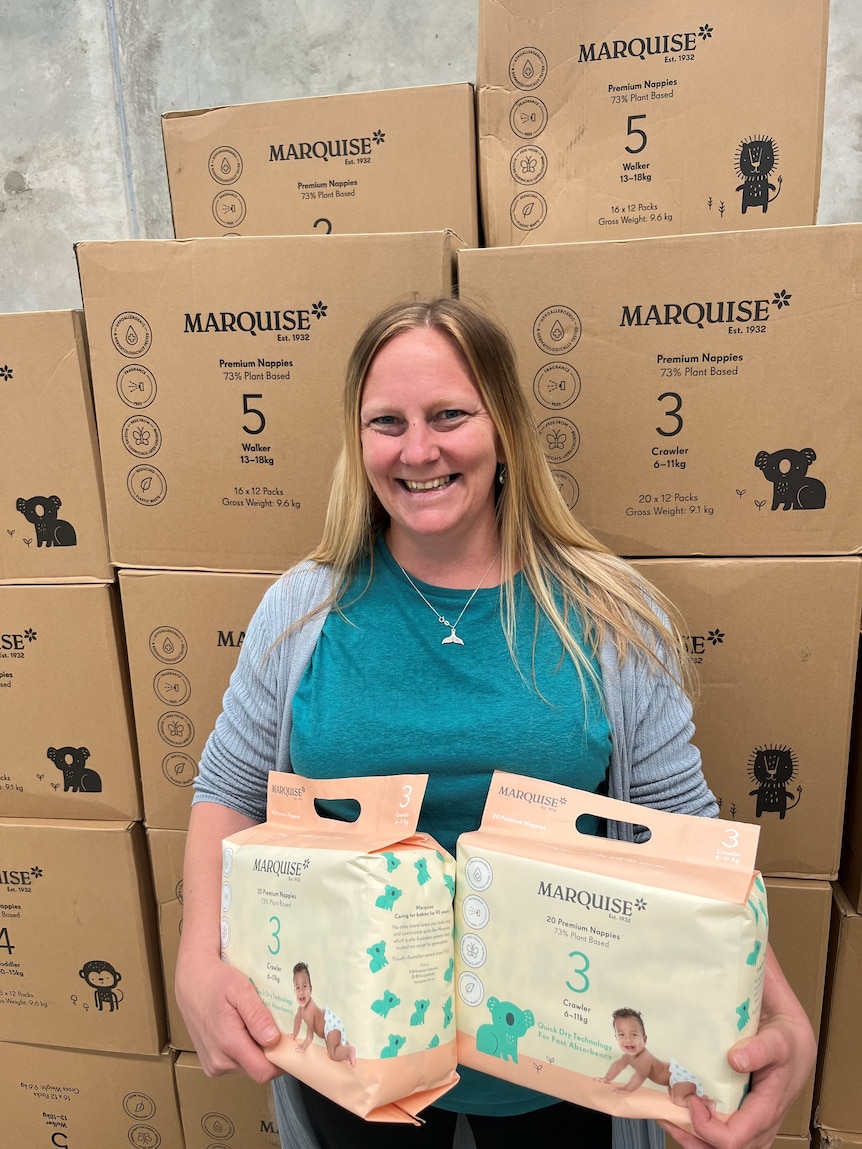 A woman stands in front of boxes of nappies.