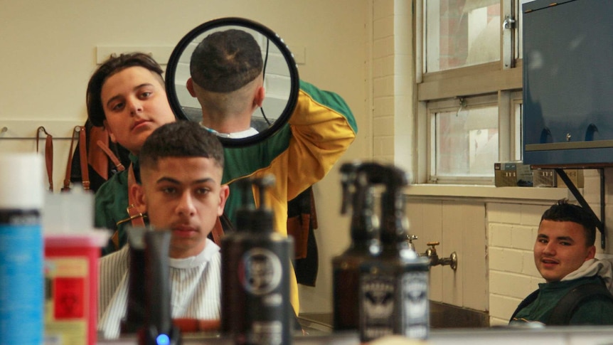 Mohomed Hamdan holds a mirror behind a 'customer', to enable him to check the back of his hair.