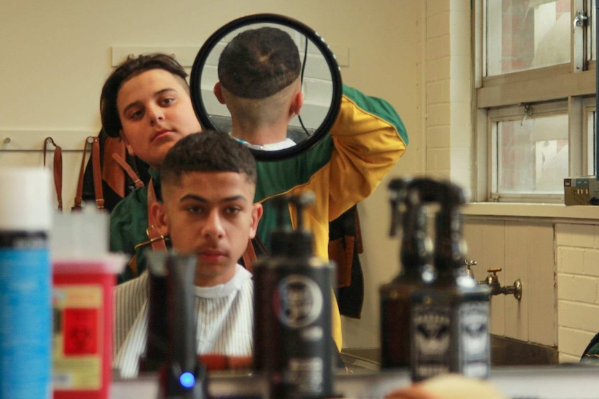 Mohomed Hamdan holds a mirror behind a 'customer', to enable him to check the back of his hair.