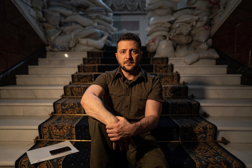 Zelenskyy sits on stairs in front of sandbags looking serious