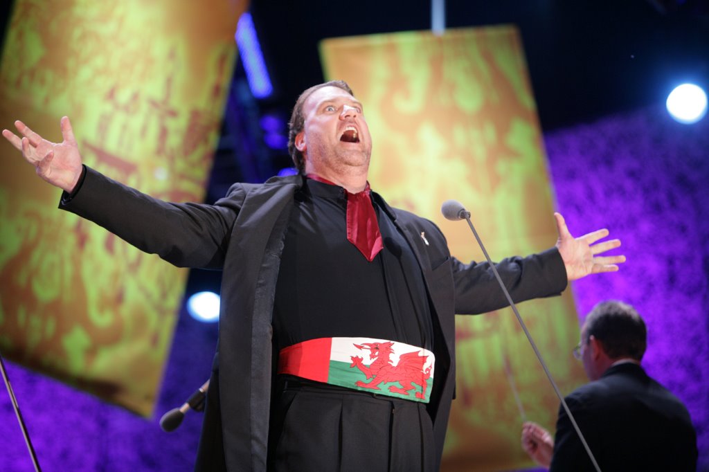 Sir Bryn Terfel performs on stage in a cummerbund of the Welsh Flag and a black suit and shirt.