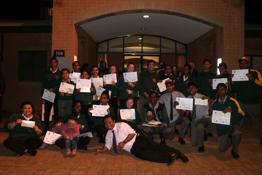 The students hold up certificates out the front of their school.