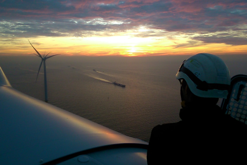 Person sitting atop wind turbine at sea.
