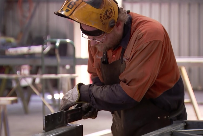 A man wearing a welder's mask works on metal