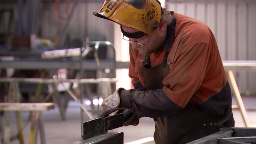 A man wearing a welder's mask works on metal