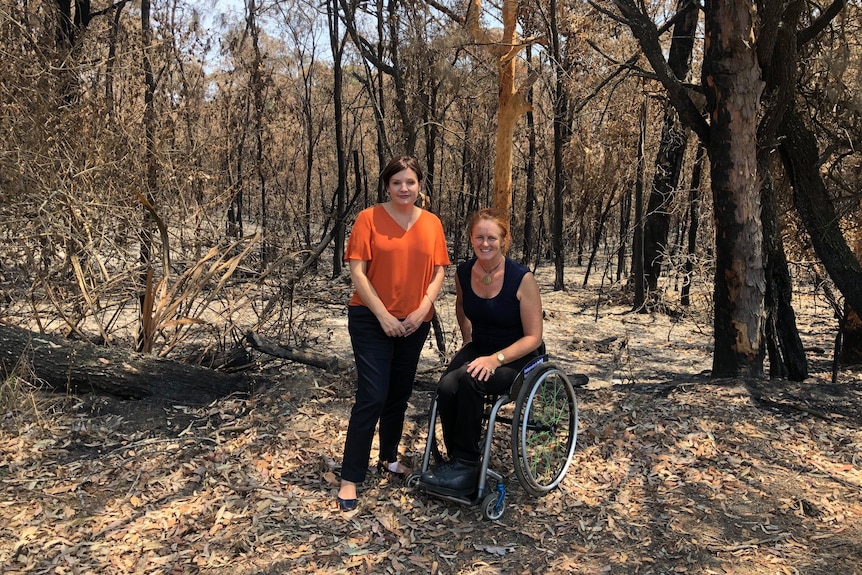 A woman standing in a red shirt in burnt bush with a woman in a wheelchair.
