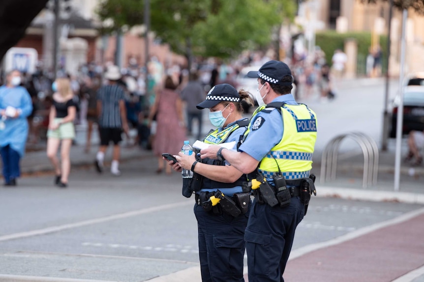 Police wear facemasks in front of a line of people wearing masks.