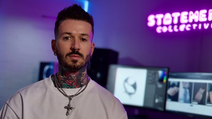 A man with face and neck tattoos sits in front of a computer