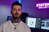 A man with face and neck tattoos sits in front of a computer