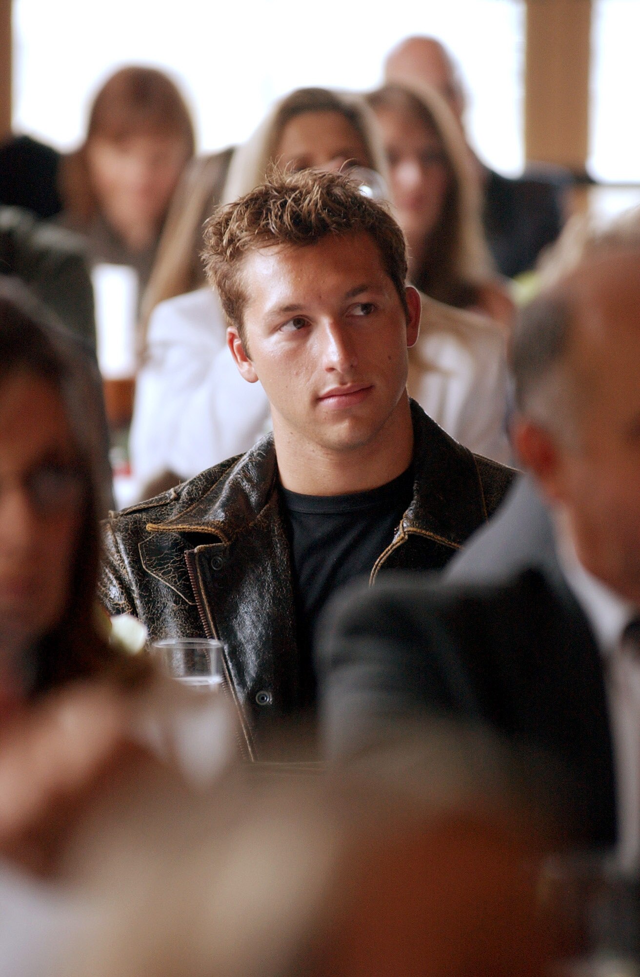 Ian Thorpe sits in a room of out-of-focus people in front and behind him. He looks off to the side thoughtfully.