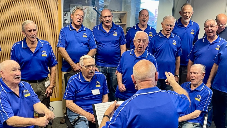Man conducts Men in choir singing in ABC Radio Studio 