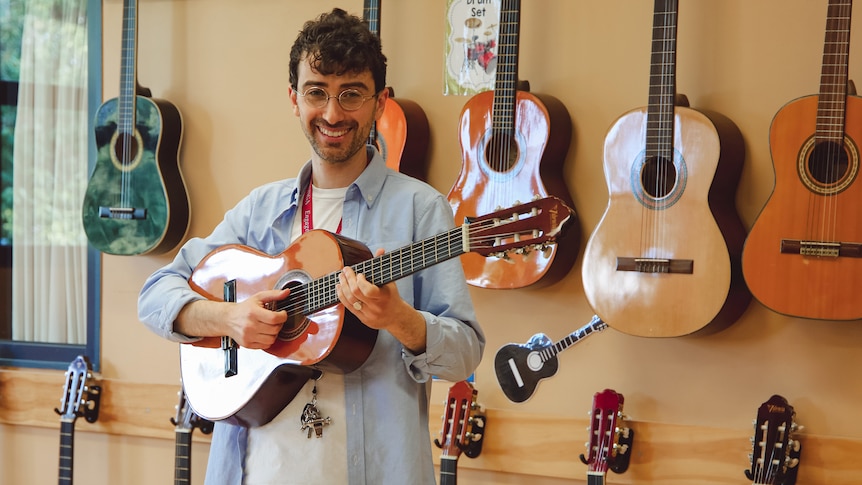 A man holding a guitar standing in front of a wall holding guitars