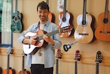 A man holding a guitar standing in front of a wall holding guitars