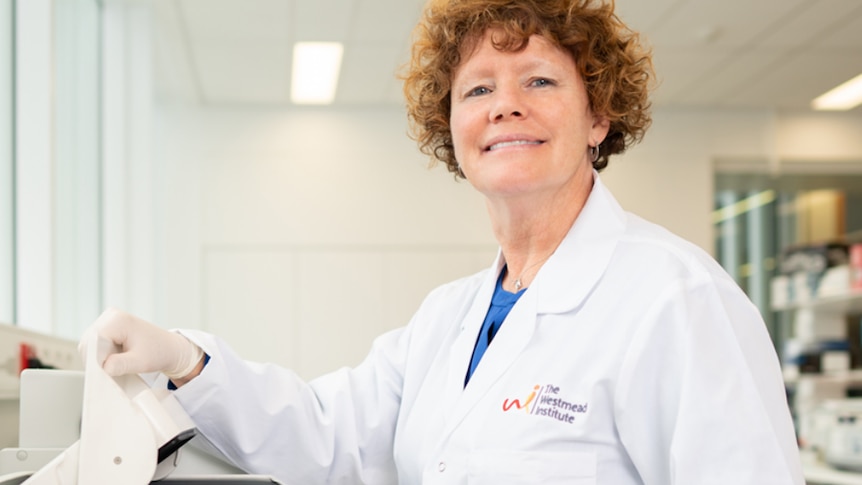 A woman in a lab coat smiles as she picks up a sample jar