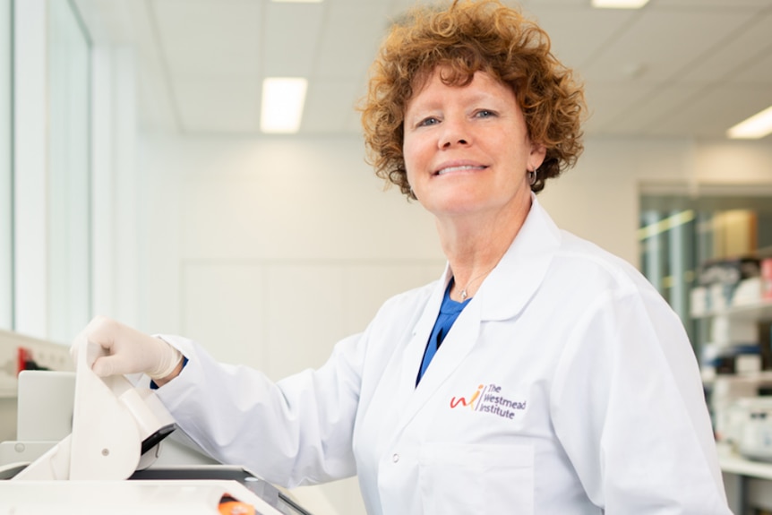 A woman in a lab coat smiles as she picks up a sample jar