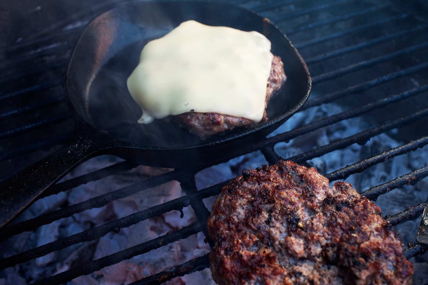 A cast iron pan on a barbeque with a burger patty with cheese for a summer bbq.