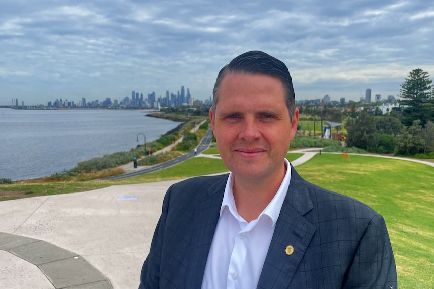 James Newbury smiles at the camera along a foreshore with the Melbourne skyline in the background.