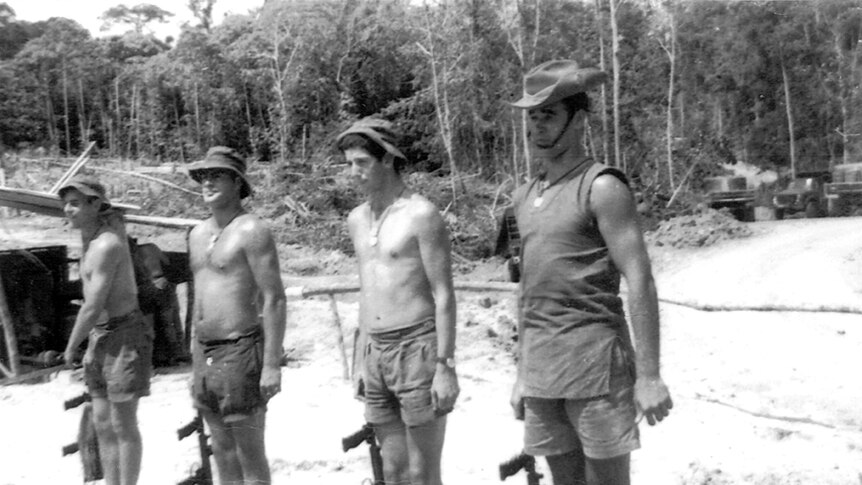 Four soldiers coming to attention on  sand in front of the jungle.